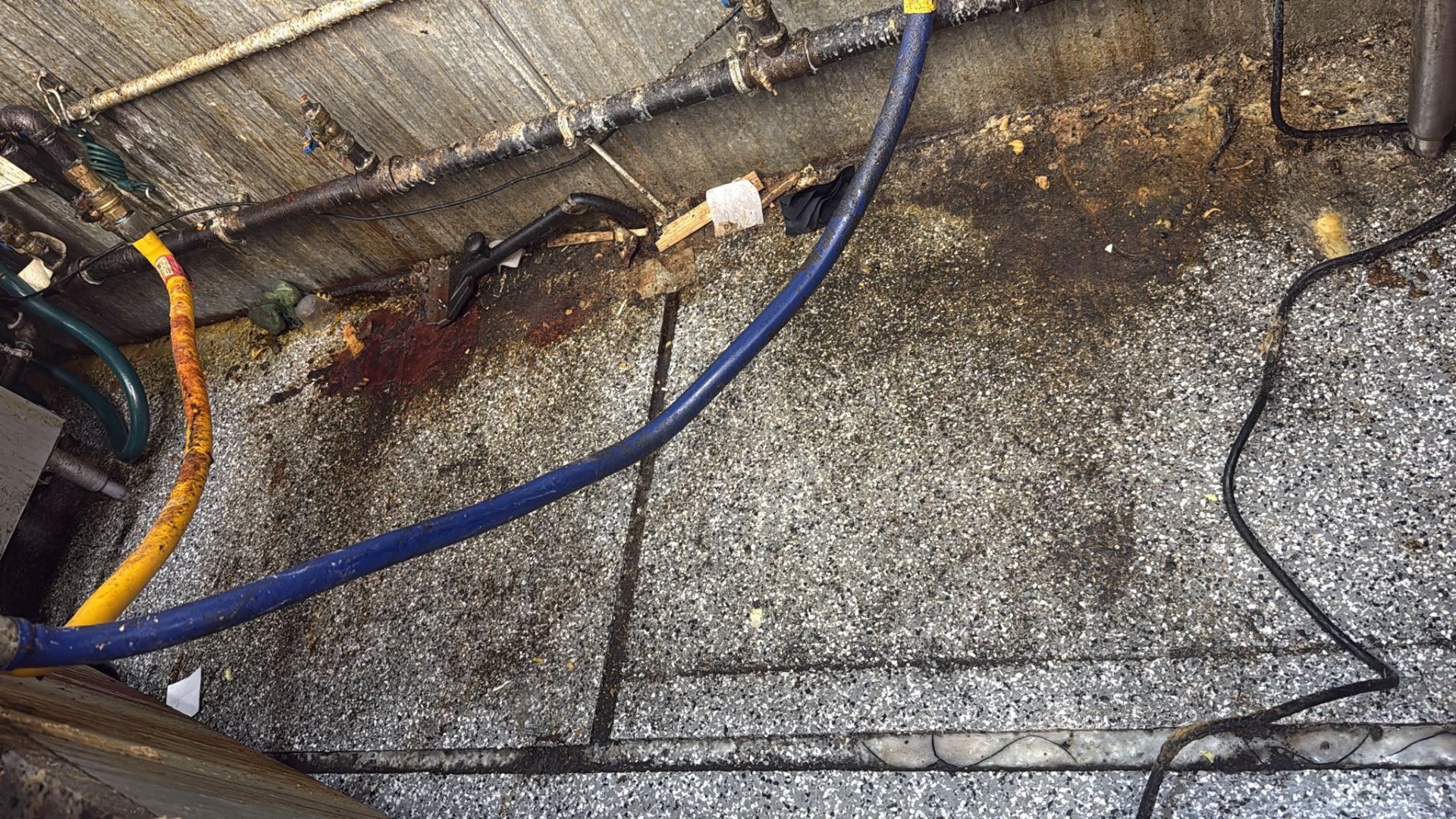 Grimy utility corner with pipes, hoses and floor debris before cleaning